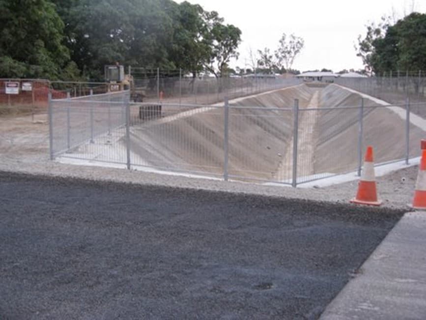 Concrete-lined flood diversion channel behind temporary fencing at Kelso