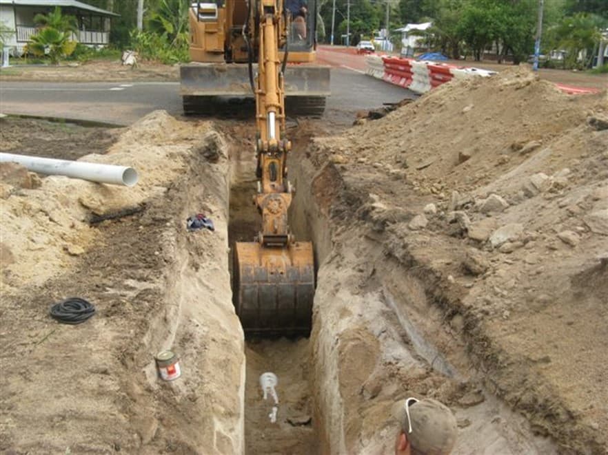 An excavator digs a sewer trench along a street at Picnic Bay