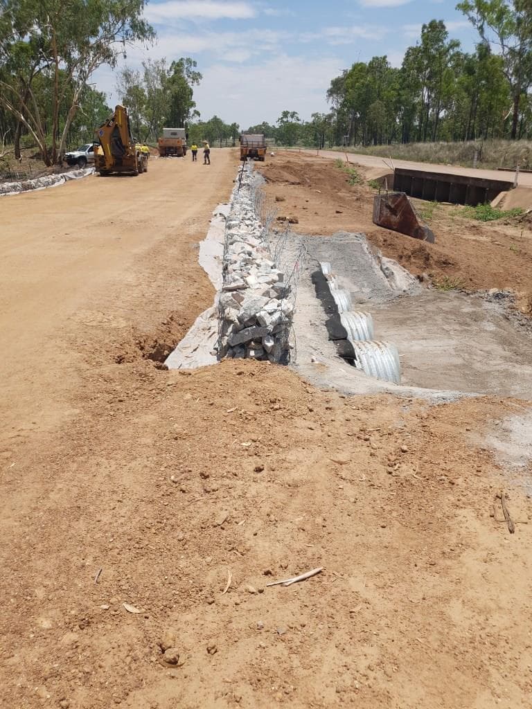 Culvert reconstruction beside the widened gravel road formation, with an excavator working beyond