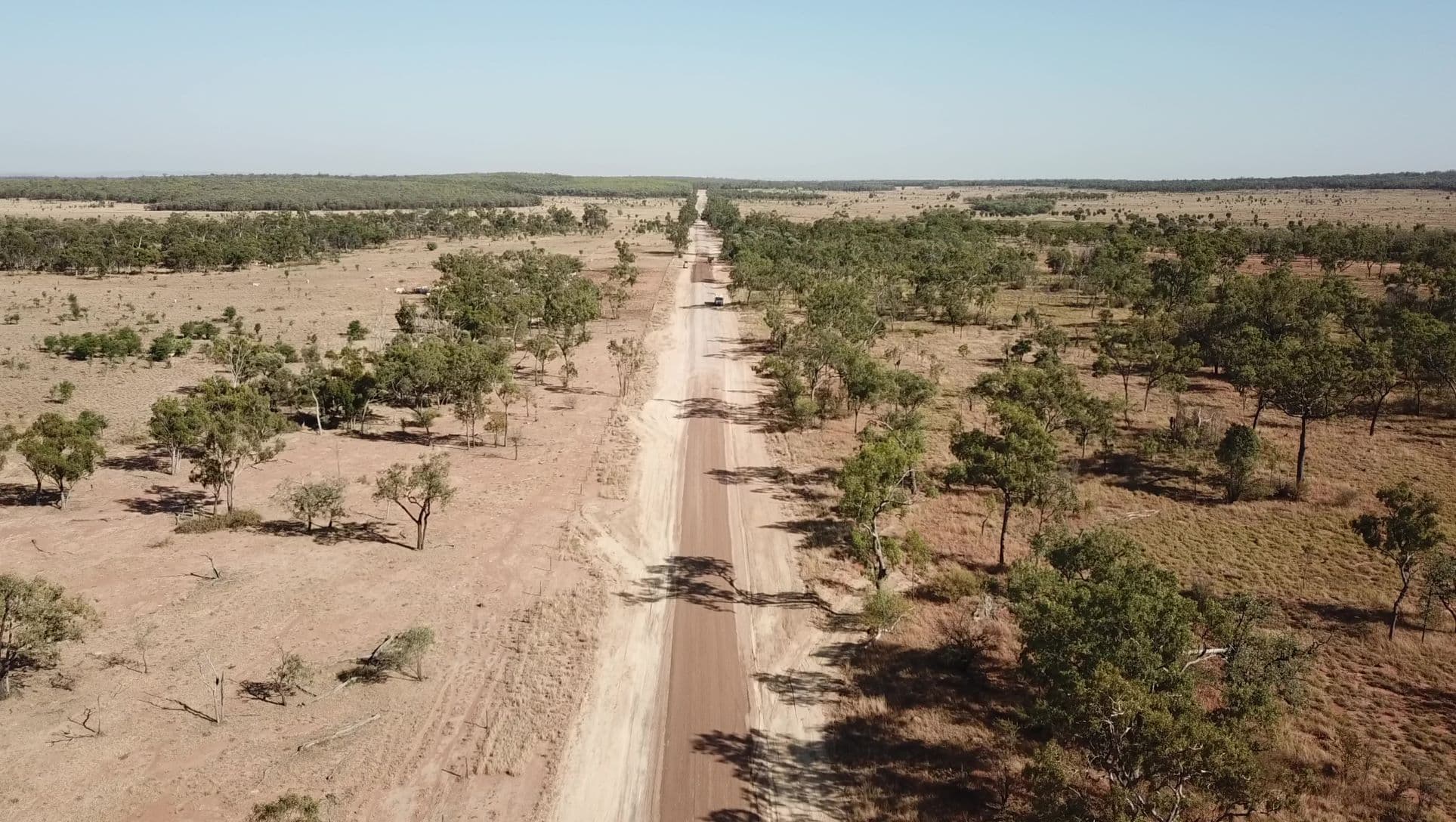 Aerial view of a long, straight rural road through open woodland