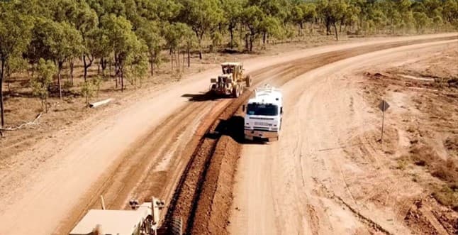 Aerial view of a grader and water truck reconstructing a gravel road through bushland